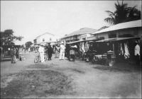 Lomé, la rue du grand-marché, vers 1910. – On aperçoit la maison dite du Dr Anthony qui, bâtie en 1904 par la firme allemande Oloff, fut vendue en 1924 comme « bien ennemi » et acquise par la famille Anthony qui la possède encore. « La ville se divise en plusieurs quartiers. Au bord de la mer se trouvent des comptoirs ; il y en a quatorze à l’heure actuelle. Vers l’ouest habitent des gens qui viennent du territoire anglais, et qui se sont établis ici. Vers le sud-ouest, ce sont les habitations des haoussa, de toutes petites huttes rondes ressemblant à des ruches d’abeilles. […] La ville est organisée sur le modèle européen avec de larges rues. La rue du Marché est, jusqu’à présent, la plus belle, bordée de chaque côté par les comptoirs  des marchands ». Source : Description de Lomé en 1892 par le R. P. Shaeffer, cité par Muller, R. P. K., Histoire de l’église au Togo, Lomé, Bon pasteur, 1968.