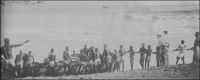 Lomé, Krumen halant une chaloupe sur la plage, vers 1900. – Les Krumen, connus comme fameux marins, sont recrutés sur la côte atlantique entre l’Ouest de la Côte d’Ivoire et le Libéria. Leurs compétences sont appréciées, tant sur les bâtiments navigant à la côte africaine, que comme équipages sédentaires chargés de faire franchir la barre aux escales. Avant la construction du wharf par les Allemands, entre mars 1902 et janvier 1904, marchandises et passagers débarquant à Lomé devaient affronter le péril de la barre. Tandis que les premières étaient souvent confiées aux vagues pour gagner la plage, les seconds empruntaient les chaloupes pilotées par les Krumen. La population de Lomé comptait, au dénombrement de 1900, quelques 111 Libériens, qui ne sont autres que ces Krumen formant les équipages des baleinières et autres surfboats qui allaient à la rencontre des navires au mouillage en rade foraine. 