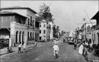 Lomé, la rue du Commerce, au début des années 1950. – La plus ancienne rue commerciale de Lomé, appelée Hamburgerstrasse du temps de la colonie allemande, regroupait la plupart des factoreries de la place, ainsi que le siège local des compagnies maritimes et de négoce. Sur la photo on distingue l’Hôtel du Golfe, suivi du bâtiment de la société John Holt de Liverpool. Un hôtel est déjà signalé dans cette rue, dans les descriptions de la ville à l’époque allemande. L’Hôtel du Golfe est explicitement mentionné  en 1941, dans l’enquête menée par les autorités militaires françaises de Lomé pour éclaircir le passage vers la colonie britannique voisine de la Gold Coast, de deux matelots de l’aviso La Gazelle.