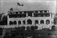Lomé, les drapeaux britannique et français flottent ensemble sur le palais du gouverneur durant la seule journée du 30 septembre 1920. –  Cérémonie de passation de pouvoir, après six ans d’occupation anglaise, la capitale du Togo doit passer, dès le lendemain, sous contrôle français. Les Allemands avaient en effet évacué Lomé le 7 août 1914, après que les gouverneurs du Gold Coast, du Dahomey et de l’AOF aient refusé leur proposition de neutraliser le Togo pour « ne pas donner aux Africains le spectacle de guerres entre Européens ». Repliés à l’intérieur des terres, les Allemands entendent utiliser leurs troupes, limitées à la force de police qui n’alignera jamais plus de 500 hommes, pour protéger la station de radio de Kamina, située à 7 km au sud-ouest d’Atakpamé.  Cette installation, qui permet de communiquer par ondes longues entre Berlin et les navires croisant dans l’Atlantique Sud, est stratégique. Malgré une résistance déterminée, et après avoir sabordé tous les équipements de Kamina, ils doivent déposer les armes le 26 août, vaincus par les troupes coloniales françaises et britanniques. Le territoire est partagé entre les alliés. Lomé est occupée par les Anglais, et le restera durant six ans jusqu’à ce qu’en 1919 un ultime partage entre alliés, entériné par la Société des Nations, attribue Lomé à la France, à compter du 1er octobre 1920. – Photo Alex Accolatsé, négatif sur verre.